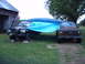 1988 Ford Bronco - Two trucks are partially covered by a blue tarp in a grassy area next to a barn.