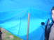 1988 Ford Bronco - A person's face and a vehicle door are partially visible beneath a blue tarp, obscuring most of the vehicle.