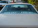 1985 Ford Crown Victoria LTD - The rear of a tan sedan shows a large white sticker on the window, with another vehicle parked nearby.