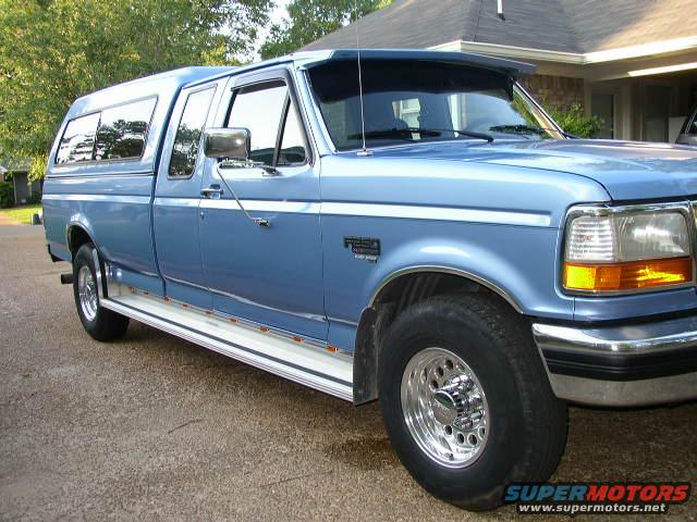 Blue pickup truck with camper shell, 3/4 front view, chrome wheels, visible "F-250" badge
