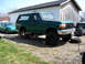 1996 Ford Bronco - A green 1996 Ford Bronco is elevated on jack stands, showing its lifted suspension and off-road tires, with another vehicle parked nearby.