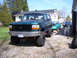 1996 Ford Bronco - A green Ford Bronco with a lifted suspension and oversized tires is parked in a driveway with other vehicles.