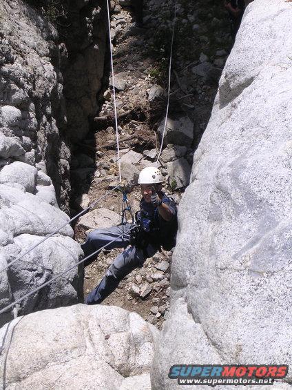 Person in helmet and harness rappelling down a rocky canyon with ropes