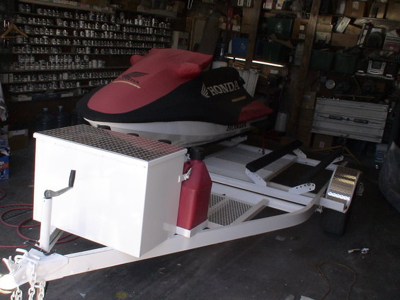 Jet ski covered in red and black on a white trailer with a red gas can and a storage box