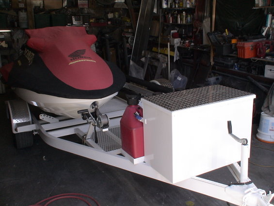 Jet ski on a trailer, covered in red and black, with a red gas can and a white storage box. Honda logo visible on cover