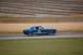 1965 Ford Mustang - A blue 1965 Ford Mustang race car speeds around a track, with grandstands in the background.