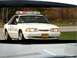 1993 Ford Mustang - A white police car with a light bar is seen from a slightly low angle.