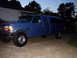 1995 Ford Bronco - Blue Ford pickup truck with a camper shell parked in a driveway at dusk.