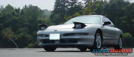 Silver 1993 Ford Probe parked outside with trees in the background. Pop-up headlights are down
