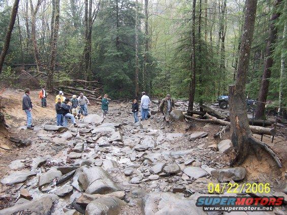 group of people on rocky, wooded trail with ATVs in background