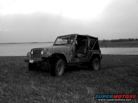Muddy Jeep Wrangler parked in a grassy field by a body of water