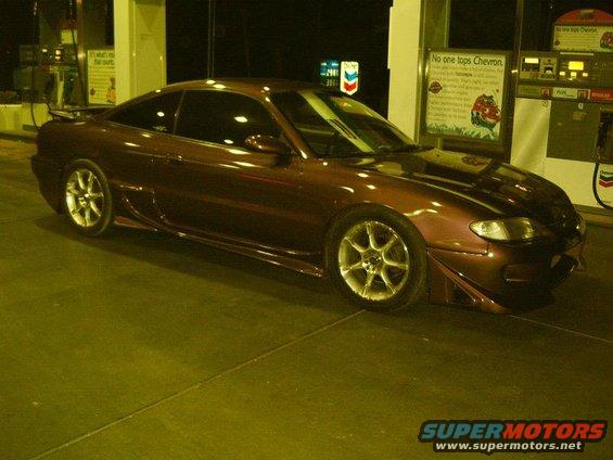 1993 Mazda MX-6 at a gas station, dark metallic paint, aftermarket wheels