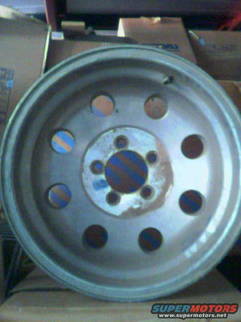 Silver metal wheel with circular cutouts and a blue and orange striped center cap