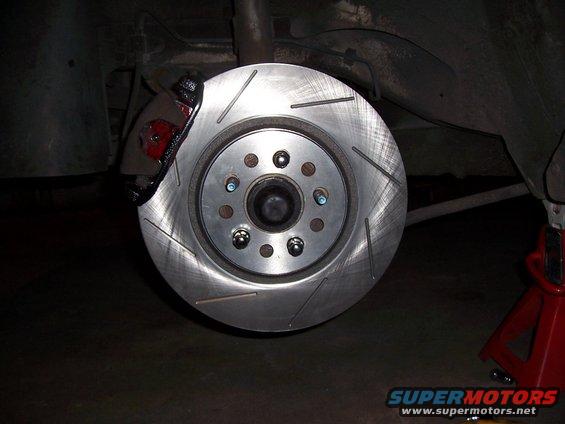 close-up of a car's rear brake rotor and caliper, with slotted rotor and red caliper
