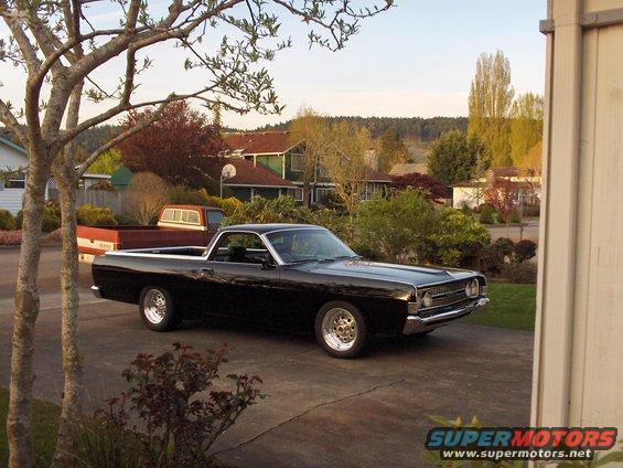 Black 1968 Ford Ranchero with chrome wheels parked in a driveway, seen from the front-right