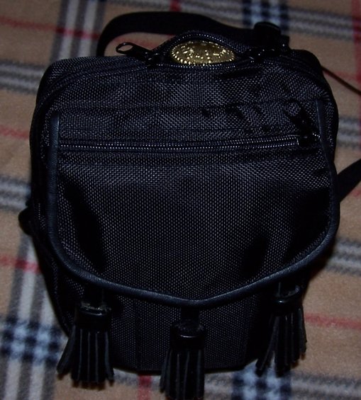 Black fabric pouch with leather trim, three tassels, and a circular gold emblem on top