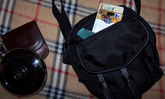 Black fabric organizer bag with credit cards and a green pocket knife visible in the main compartment; a brown leather coin purse and a round metallic object are to the left