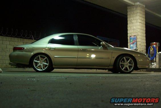 Gold sedan parked at night, side view. Looks like a 1998 Mercury Sable