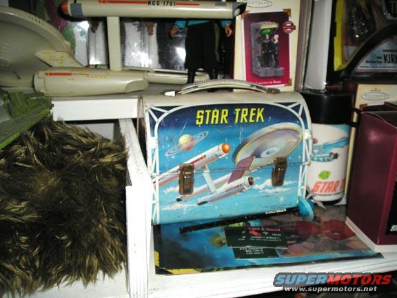 Star Trek lunchbox with Enterprise graphic, NCC-1701 model, and other collectibles on a shelf