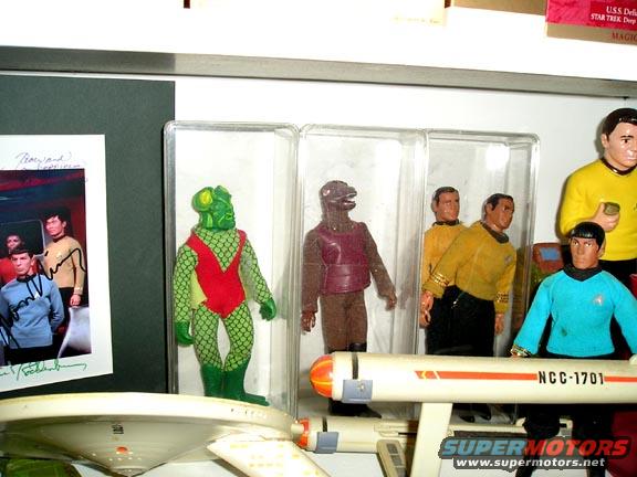 Star Trek action figures, including a green alien and crew members, displayed with a model USS Enterprise ship