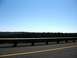 1969 Mercury Cougar - A view of a highway guardrail with a thick forest stretching across the horizon under a bright, cloudless sky.