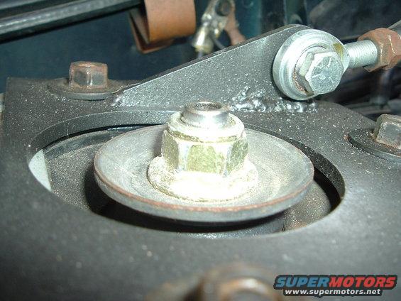 Close-up of a suspension strut mount with a large nut and washer, showing metal components and bolts