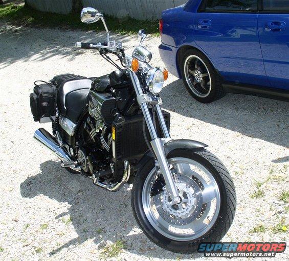 Black motorcycle front wheel and suspension with a blue car in the background