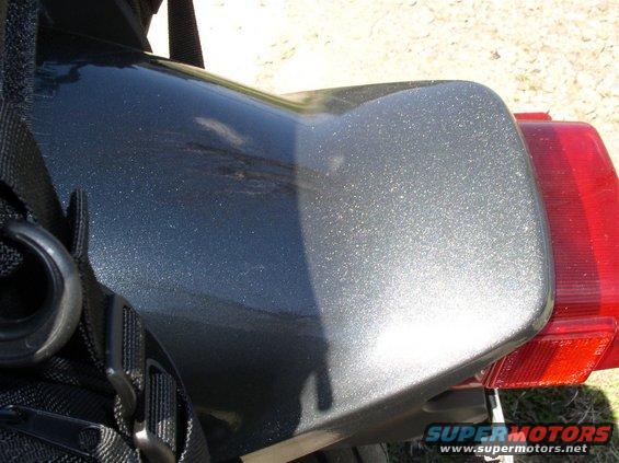 Close-up of a dark metallic motorcycle tail section with a red taillight visible