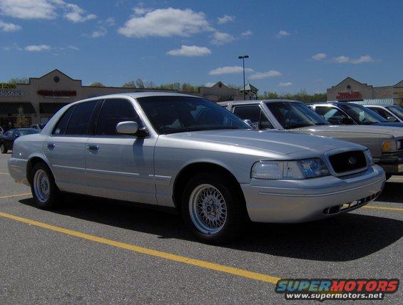 Silver 2002 Ford Crown Victoria parked in a lot, front passenger side visible. Other cars are parked nearby