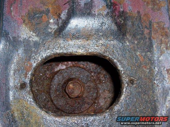 Close-up of a rusty metal bracket with a bolt and washer visible through an opening