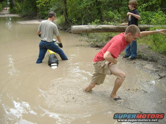 Motorcycle stuck in muddy water with people trying to push it