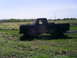 1994 Ford F-250 - A pickup truck is covered in mud while sitting in a grassy field under a clear sky.