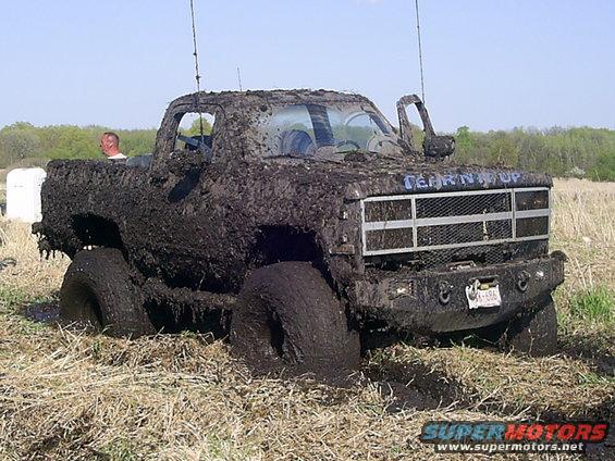 Mud-covered pickup truck with 'TEARIN' IT UP' on grille stuck in field