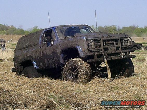 Mud-covered GMC SUV stuck in a grassy field, front grille visible
