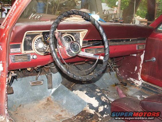 Interior of a red car with a cracked steering wheel and worn dashboard. The floor is dirty and peeling