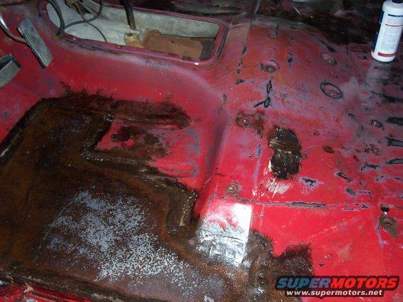 rusted out floor pan of a vehicle, showing significant rust damage and some patched areas