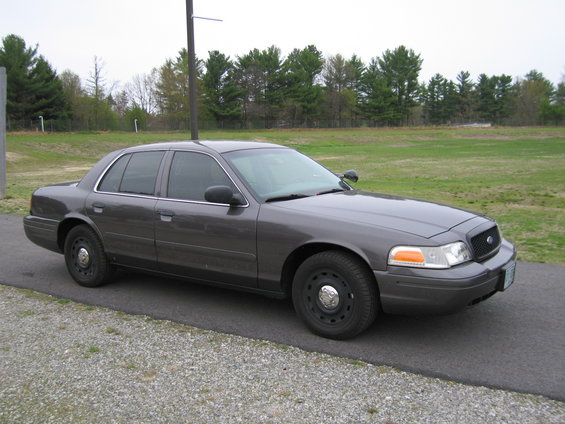 Dark gray Ford Crown Victoria parked on asphalt next to a gravel shoulder