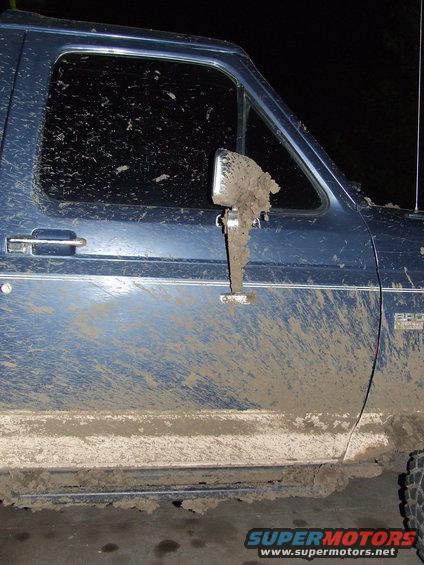 Mud-splattered driver's side door and side mirror of a blue 1986 Ford Bronco