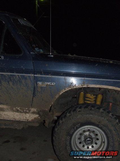 Mud-splattered blue Ford Bronco with yellow shocks, seen from the front quarter