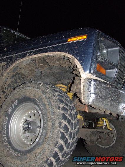 Mud-covered blue Ford Bronco front fender and tire, showing yellow suspension components