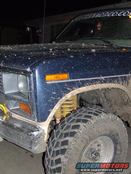 Mud-covered 1986 Ford Bronco front fender, headlight, and tire. Yellow shock absorber visible