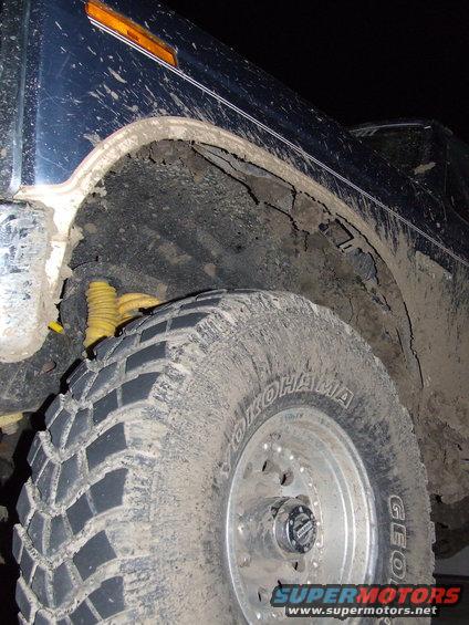 Mud-covered 1986 Ford Bronco front wheel well and Yokohama tire. Yellow shock absorber visible