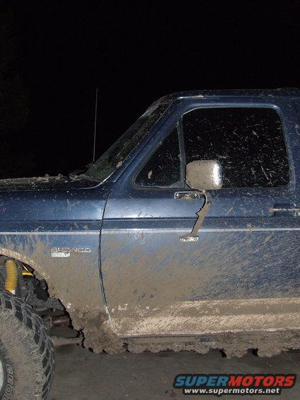 Blue 1986 Ford Bronco side view, covered in mud, with yellow shock absorber visible