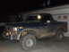 1986 Ford Bronco - This heavily muddied blue Ford Bronco is parked in front of a garage at night.