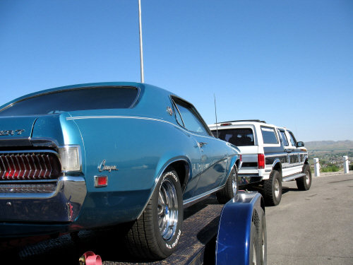 Blue 1969 Mercury Cougar XR7 on a trailer, rear view, with a white and black SUV behind it