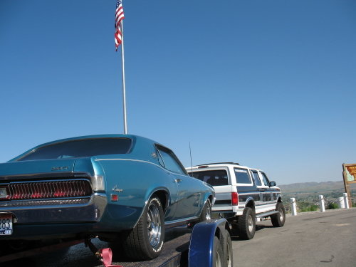 Rear view of a blue 1970 Mercury Cougar on a trailer, with an American flag flying overhead