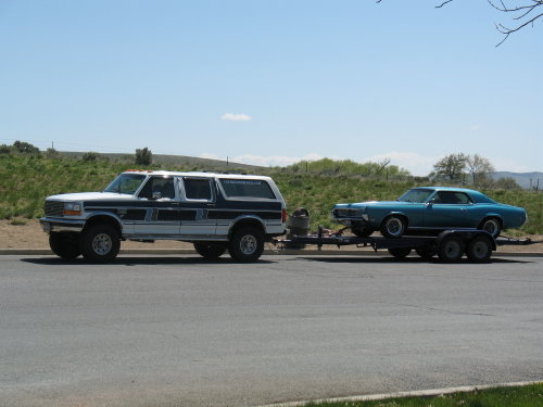 Teal 1969 Mercury Cougar on a trailer towed by a white and blue Ford Bronco