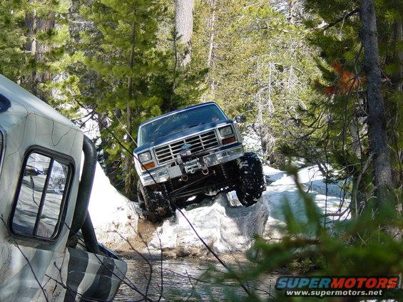 Blue Ford Bronco climbing rocks with a winch, front-left tire off the ground