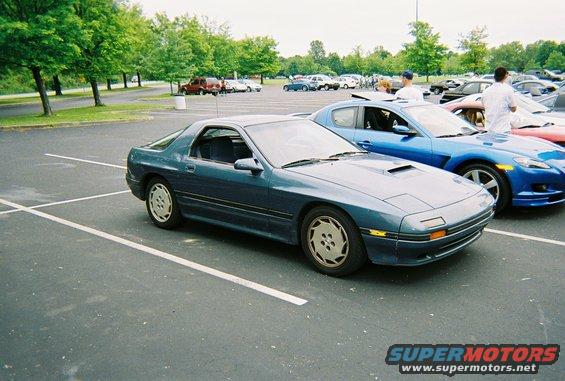 Blue coupe with pop-up headlights and distinctive five-spoke wheels parked in a lot