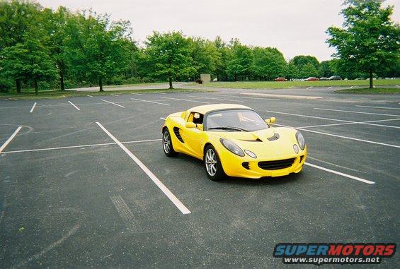 Yellow sports car parked in an empty lot with trees in the background